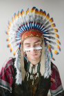 Young man with line on face posing in traditional Native American costume with eyes closed — Stock Photo