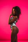 Smiling young black woman in bodysuit posing on pink background with eyes closed. — Stock Photo