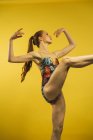 Vista lateral de bailarina de ballet con la pierna levantada sobre fondo amarillo - foto de stock