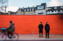 Двое мужчин в теплой одежде стоят у оранжевой стены на улице . — стоковое фото
