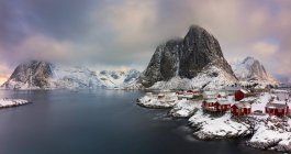 Panoramic view of lake with red village houses at shore in winter mountains — Stock Photo