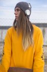 Junges Mädchen mit Kopfhörern posiert mit Longboard in der Hand und schaut auf Straßenszene weg — Stockfoto