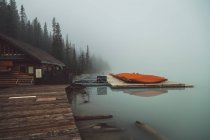 Casa in legno vicino al molo sul lago nebbioso — Foto stock