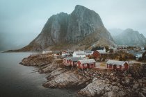 Landscape of rocky shore with village houses at foggy mountains . — Stock Photo