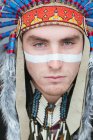 Portrait of man with painted line on face posing in traditional Native American costume and looking at camera — Stock Photo