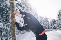 Вид сзади женщины, опирающейся на столб и согревающей мышцы зимой на обочине дороги — стоковое фото