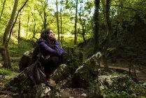 Вид збоку на туристичну жінку, що сидить на камені в лісі та відпочиває . — стокове фото