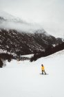 Tourist in yellow jacket riding snowboard on snowy mountain slope. — Stock Photo