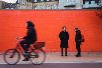 Two men standing at orange wall on side walk — Stock Photo