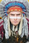 Портрет людина з розписом лінії на обличчі постановки в традиційних американських індіанців костюм і, дивлячись на камеру — стокове фото
