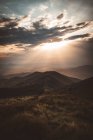 Luz solar penetrando nuvens escuras sobre colinas paisagem — Fotografia de Stock
