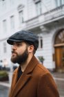 Side view of confident man in cap and coat walking at street — Stock Photo