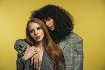 Zwei Frauen umarmen sich und blicken in die Kamera auf gelbem Hintergrund — Stockfoto