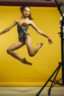 Ballet dancer jumping on yellow background while dancing in studio. — Stock Photo