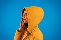 Smiling woman in yellow hood posing against blue background — Stock Photo