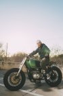 Vue latérale de l'homme posant sur la moto au coucher du soleil et regardant la caméra — Photo de stock