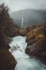 Kleiner Gebirgsfluss vor dem Hintergrund eines Wasserfalls in nebligen Hügeln. — Stockfoto