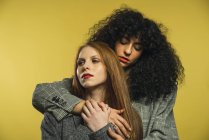 Two young women embracing together on yellow background. — Stock Photo