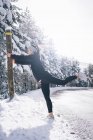Seitenansicht des Anlehnens an Pfosten und Aufwärmen der Muskeln auf verschneiter Landstraße — Stockfoto