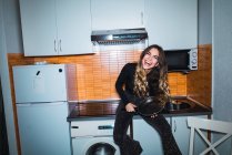 Сміється жінка сидить на кухонному столі з сковородою в руках — стокове фото