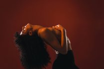 Vista lateral de la mujer topless rizado posando sobre fondo rojo en el estudio . - foto de stock