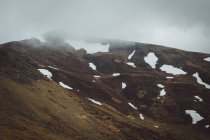 Montagna verde con neve sotto il cielo nebbioso — Foto stock