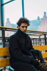 Portrait of pensive young man sitting on bench at station — Stock Photo