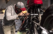 Vue latérale du mécanicien réparant la moto personnalisée à l'atelier — Photo de stock