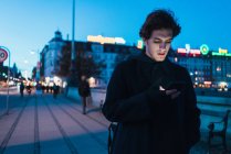 Мужчина просматривает смартфон на вечерней улице — стоковое фото