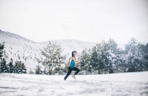 Vista lateral da mulher correndo no campo nevado — Fotografia de Stock