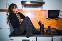 Seitenansicht einer jungen Frau am Küchentisch — Stockfoto