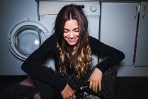 Smiling woman sitting at laundry machine and looking down — Stock Photo