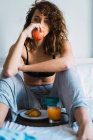 Привлекательная женщина с яблоком сидит на подносе для завтрака на кровати — стоковое фото