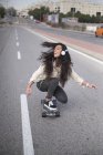 Menina alegre em fones de ouvido montando longboard na cena de rua — Fotografia de Stock