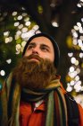 Porträt eines bärtigen Mannes, der gegen Weihnachtsbeleuchtung posiert — Stockfoto