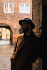Bearded man in coat leaning on wall at arch — Stock Photo