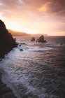 Vue sur la côte rocheuse et les vagues de l'océan dans les lumières du coucher du soleil . — Photo de stock