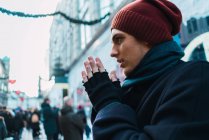 Side view of man in hat rubbing hands to warm at street scene — Stock Photo