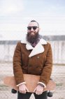 Портрет бородатого чоловіка в сонцезахисних окулярах, що тримає скейтборд — стокове фото