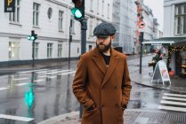 Bearded man in coat posing by traffic light at street scene — Stock Photo