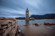 Torre de sino submersa em lago calmo sob paisagem dramática — Fotografia de Stock