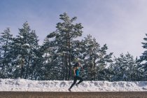Side view of fit woman running along snowy woods — Stock Photo
