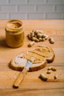 Vista de cerca del sándwich de mantequilla de cacahuete que se prepara en la mesa con cacahuetes y frasco - foto de stock