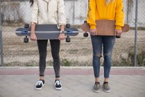 Vista basso angolo di due ragazze in posa con longboard in strada — Foto stock