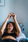 Сміється жінка лежить на ліжку і переглядає смартфон — стокове фото