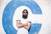 Bearded man posing with arms crossed and leaning on wall on street — Stock Photo