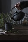 Mão de colheita de chá derramando de panela oriental para xícara na mesa . — Fotografia de Stock