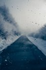 Asphalt road in winter forest seen through glass with water drops. — Stock Photo