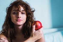 Retrato de mujer sentada con manzana y mirando a la cámara - foto de stock