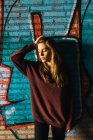 Young woman holding head and and leaning at brick wall with graffiti. — Stock Photo